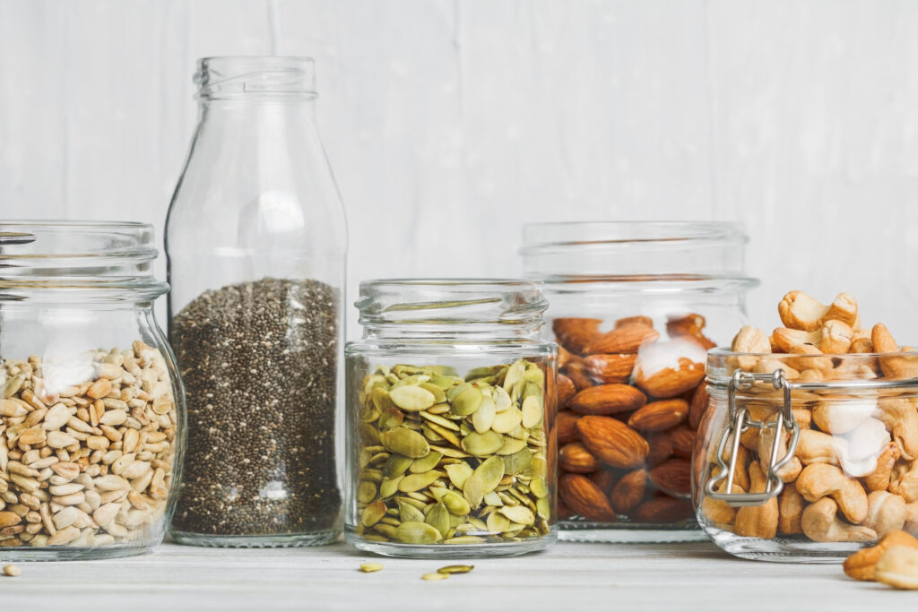Various nuts and seeds in glass jars over white wooden table against white background. 