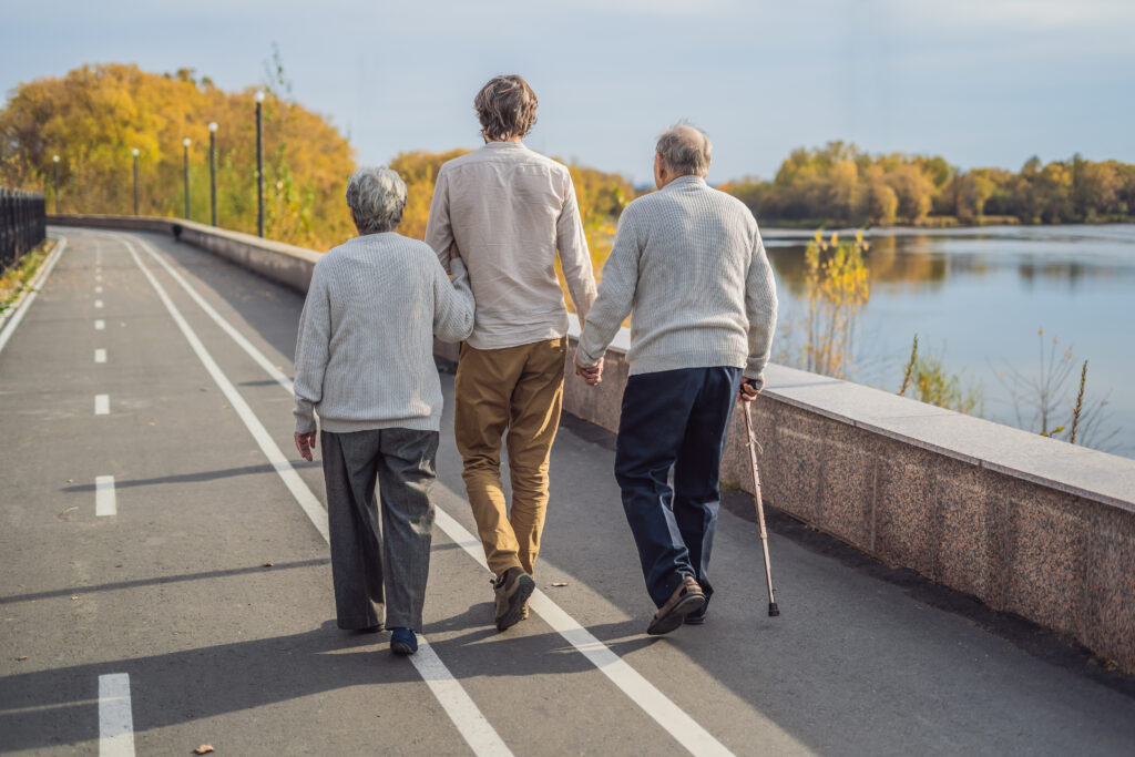 An elderly couple walks in the park with a male assistant or adult grandson. 