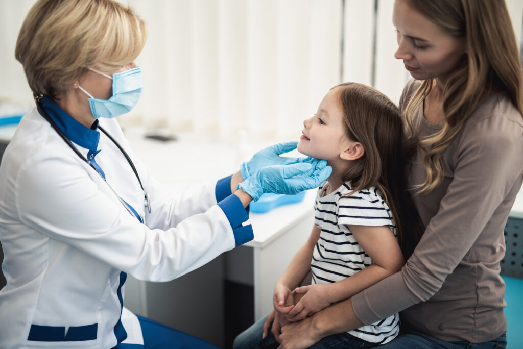 Pediatrician woman examining tonsils of smiling little girl in medical office