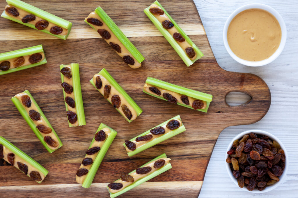 Homemade ants on a log with celery, peanut butter and raisins on a wooden board, top view.