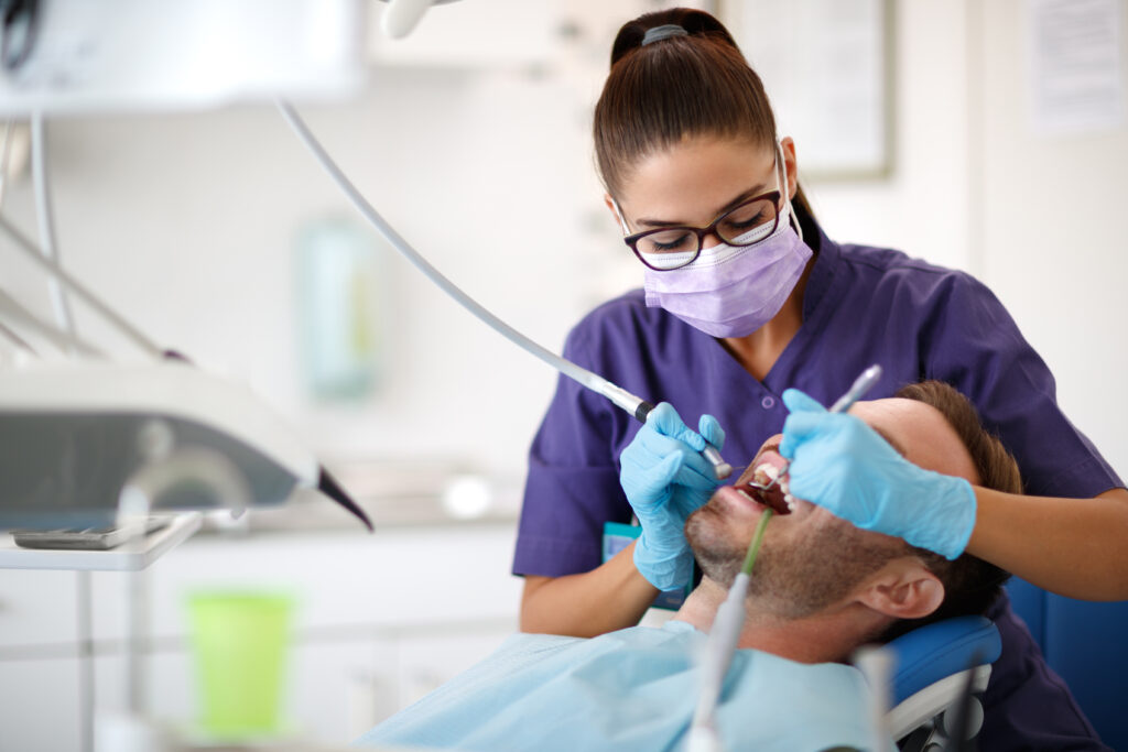 Young female dentist drilling tooth to patient in dental clinic