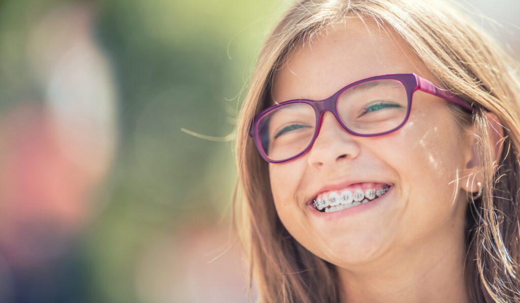 Portrait of a happy smiling teenage girl with dental braces and glasses.