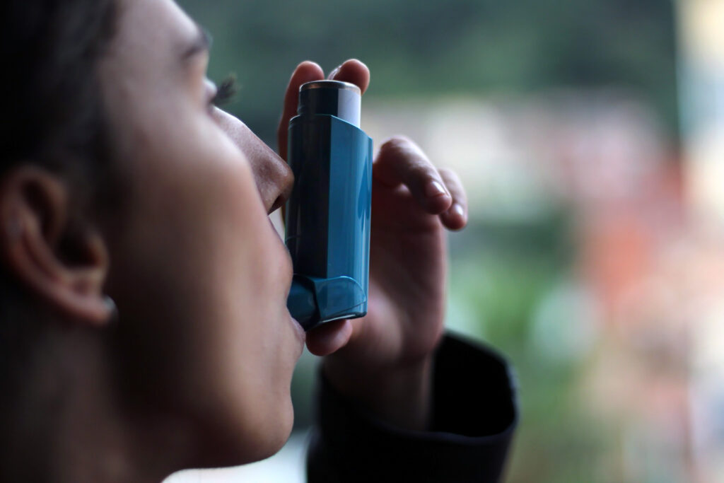 Health and medicine - Young girl using blue asthma inhaler to prevent an asthma attack. Pharmaceutical product to prevent and treat asthma.