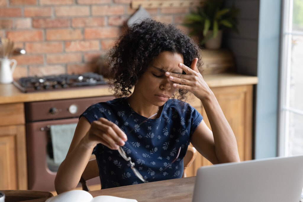 Young woman working on laptop at home touching her eyes in discomfort