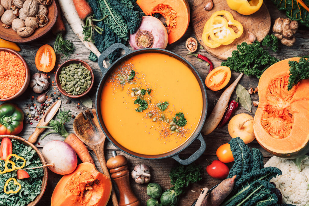 Squash soup and other winter vegetables arranged on a wooden surface, seen from above